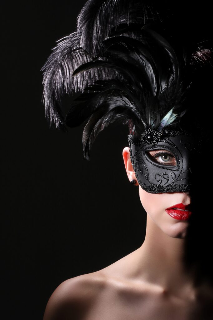 Eine Frau mit einer aufwendigen schwarzen Maske und roten Lippen, teilweise im Schatten, was eine geheimnisvolle und verführerische Stimmung erzeugt.