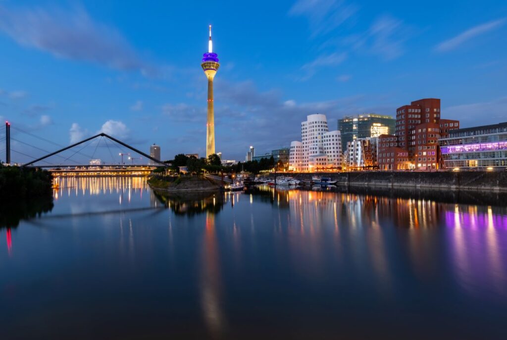 Die beleuchtete Skyline von Düsseldorf mit dem Fernsehturm und dem Medienhafen spiegelt sich im Rhein – perfekt für ein Treffen mit Escort Düsseldorf.